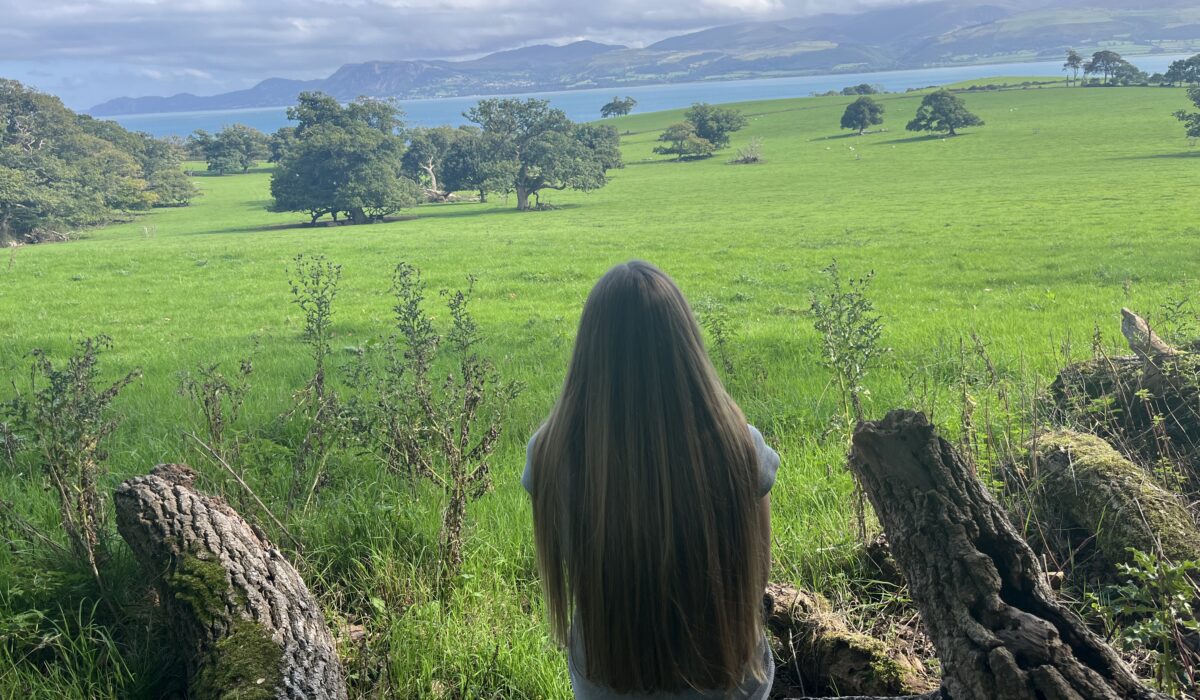 Woman sitting on a fallen tree looking across the Welsh countryside, reflecting on replaying conversations in her head